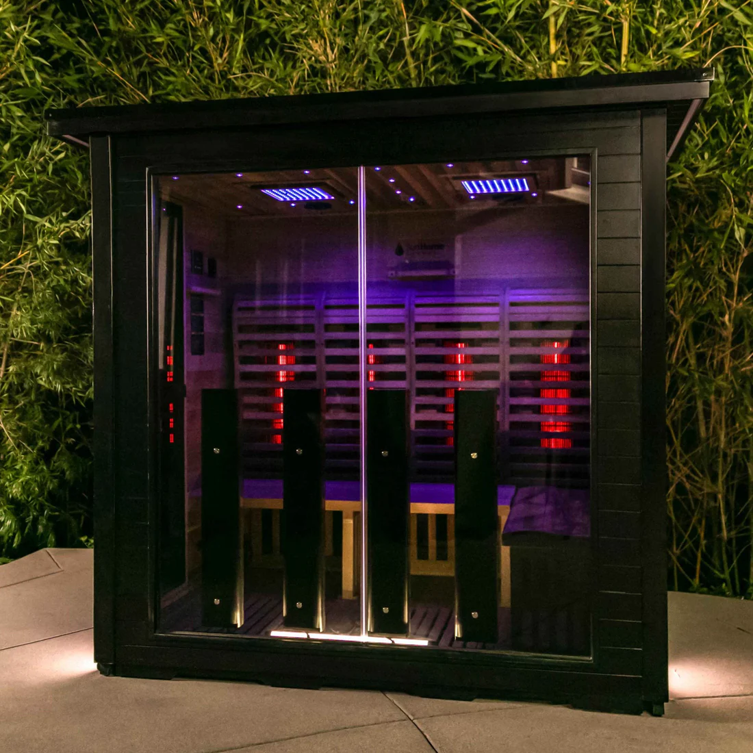 Modern outdoor sauna with colorful LED lighting inside a glass enclosure.
