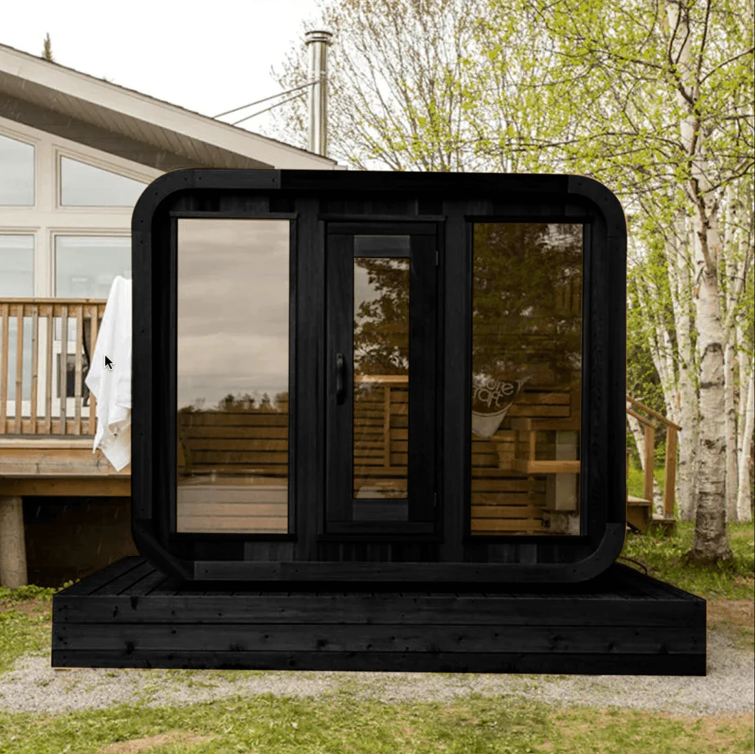A modern black tiny house with large windows on a wooden deck.