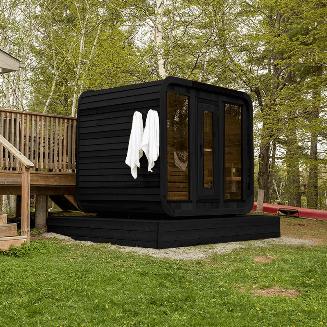 Modern black sauna cabin in a forested backyard with wooden deck.
