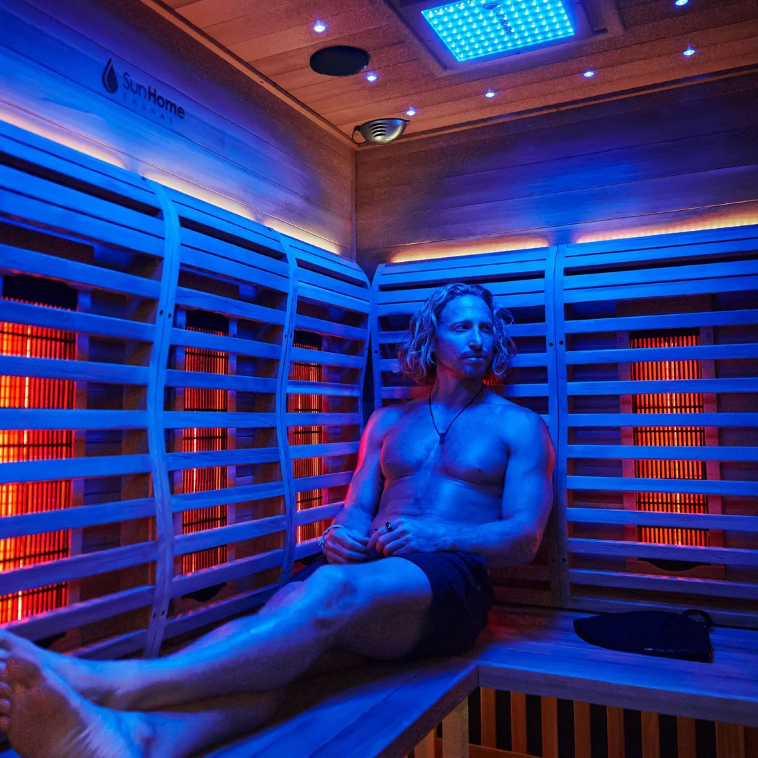 Man relaxing in an infrared sauna with blue and red lighting.