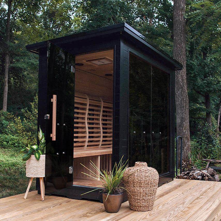 Modern outdoor sauna surrounded by trees with glass walls and wooden interior.