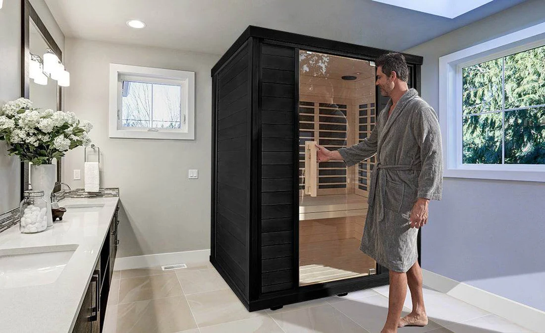 A man in a robe using a black sauna cabinet in a bathroom.