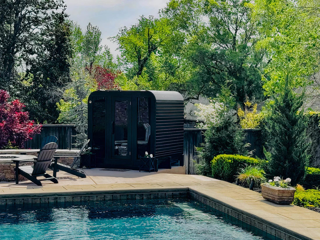 A modern black pool house near a clear swimming pool surrounded by greenery.