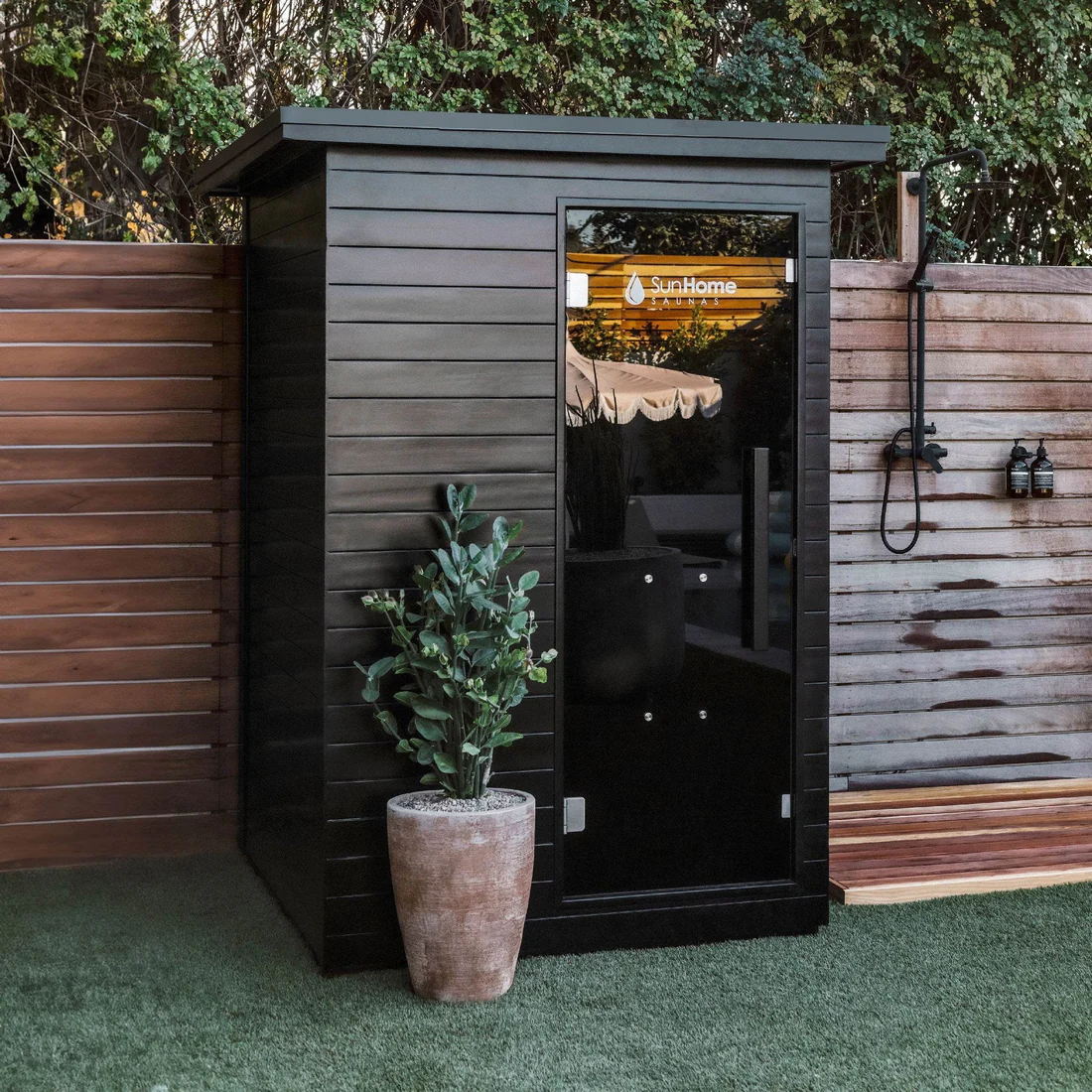 Sleek black garden shed with a potted plant beside it.