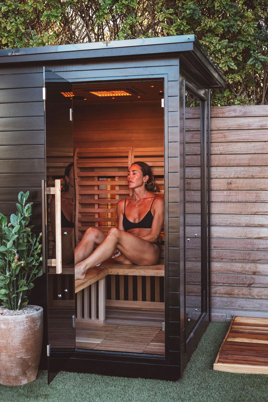 Woman relaxing in a wooden sauna wearing a black bikini.
