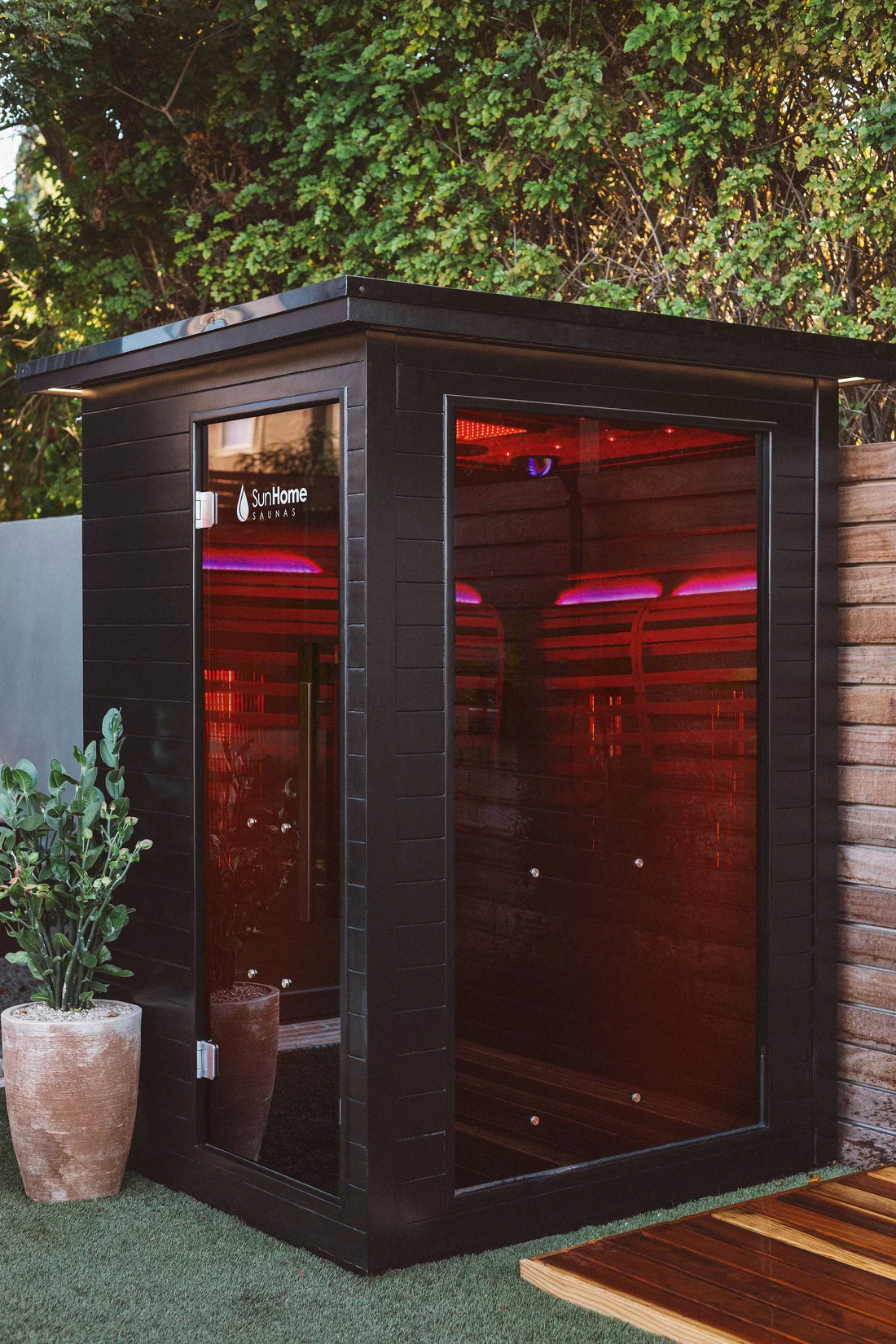 Modern outdoor sauna with dark wood and red lighting.
