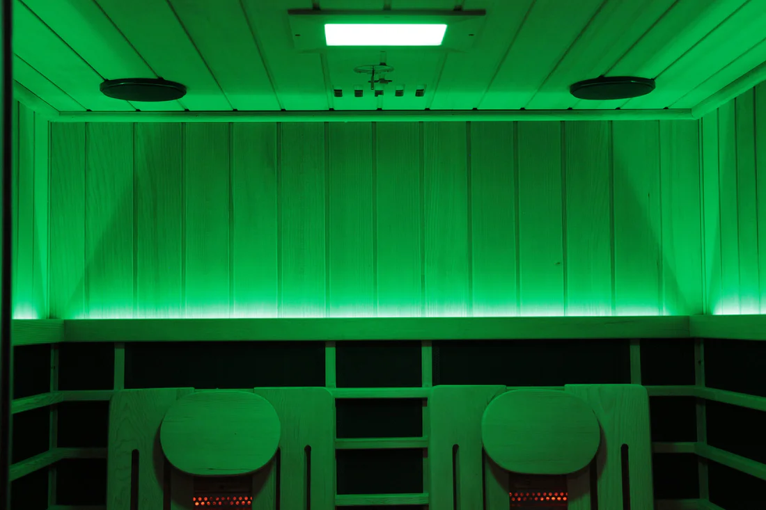 Interior of a green-lit sauna with wooden benches and ceiling.