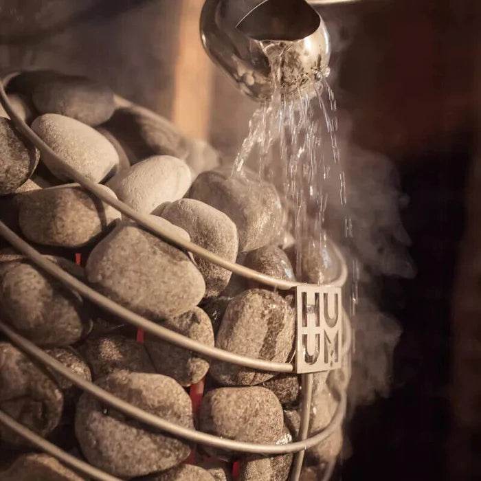 A rustic sauna stove with stones and steam rising.