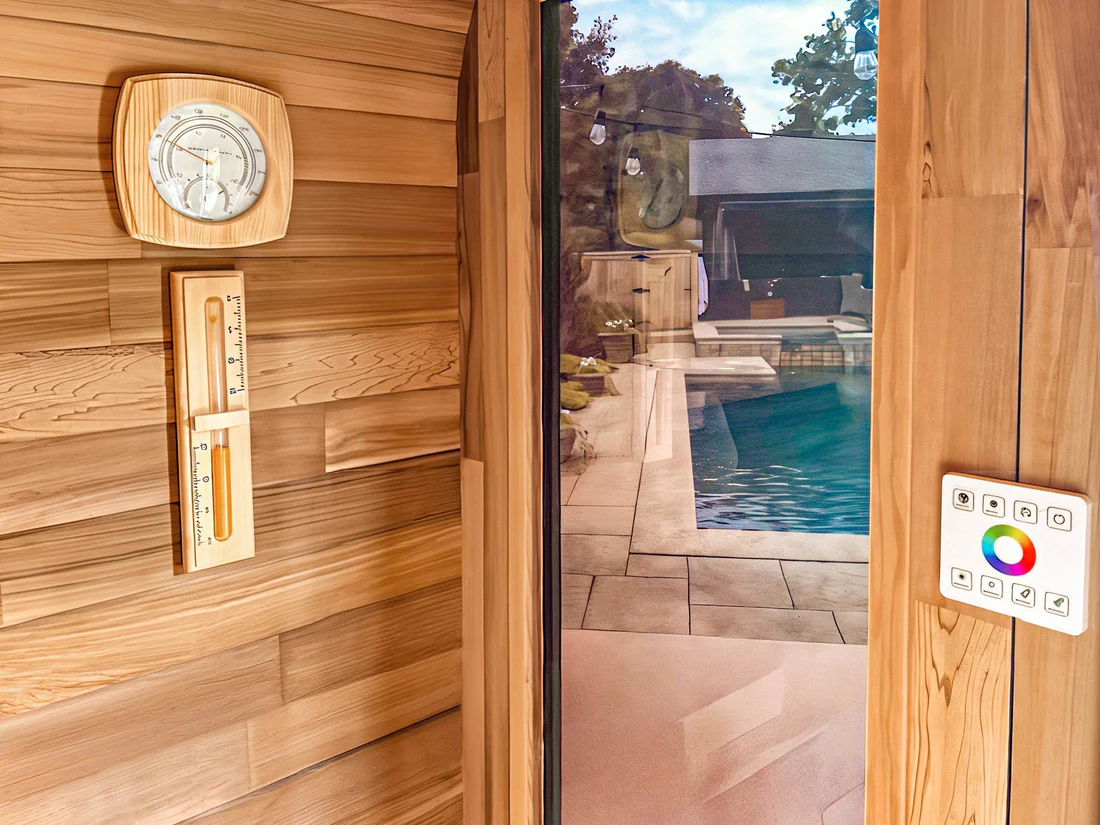 Wood-paneled sauna with a glass door overlooking a pool area.
