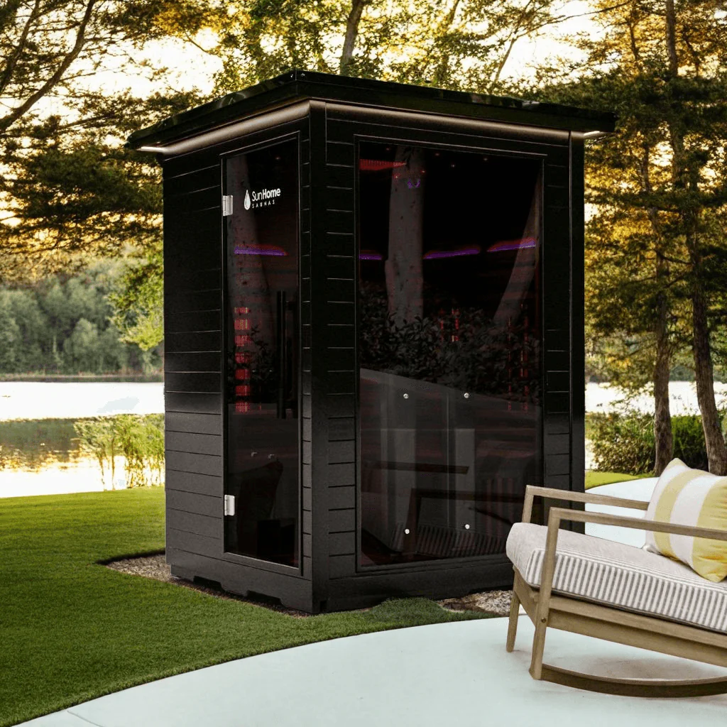 A modern outdoor sauna cabin situated by a lakeside with surrounding trees.