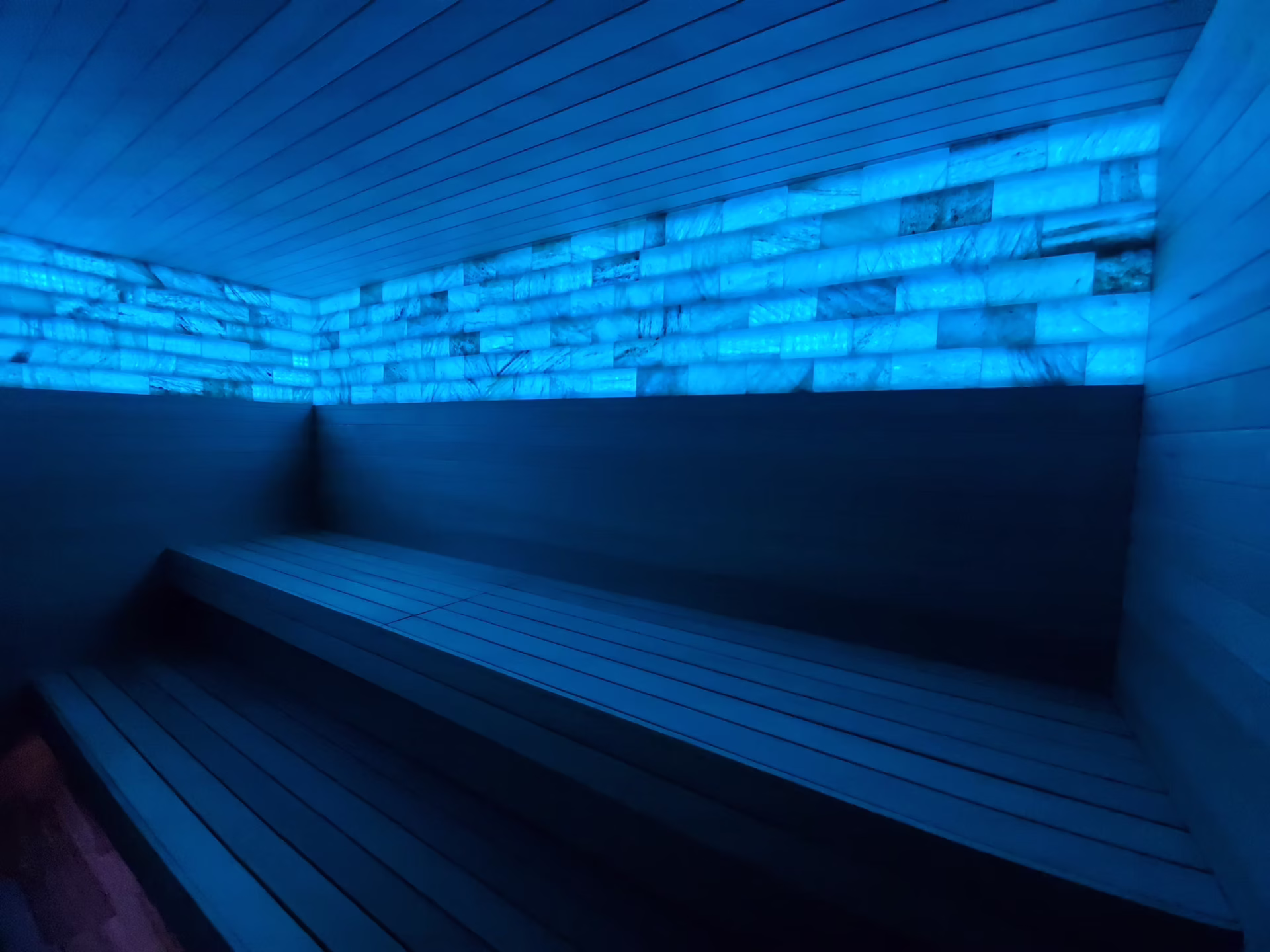 Modern sauna with blue LED lighting and wooden benches.