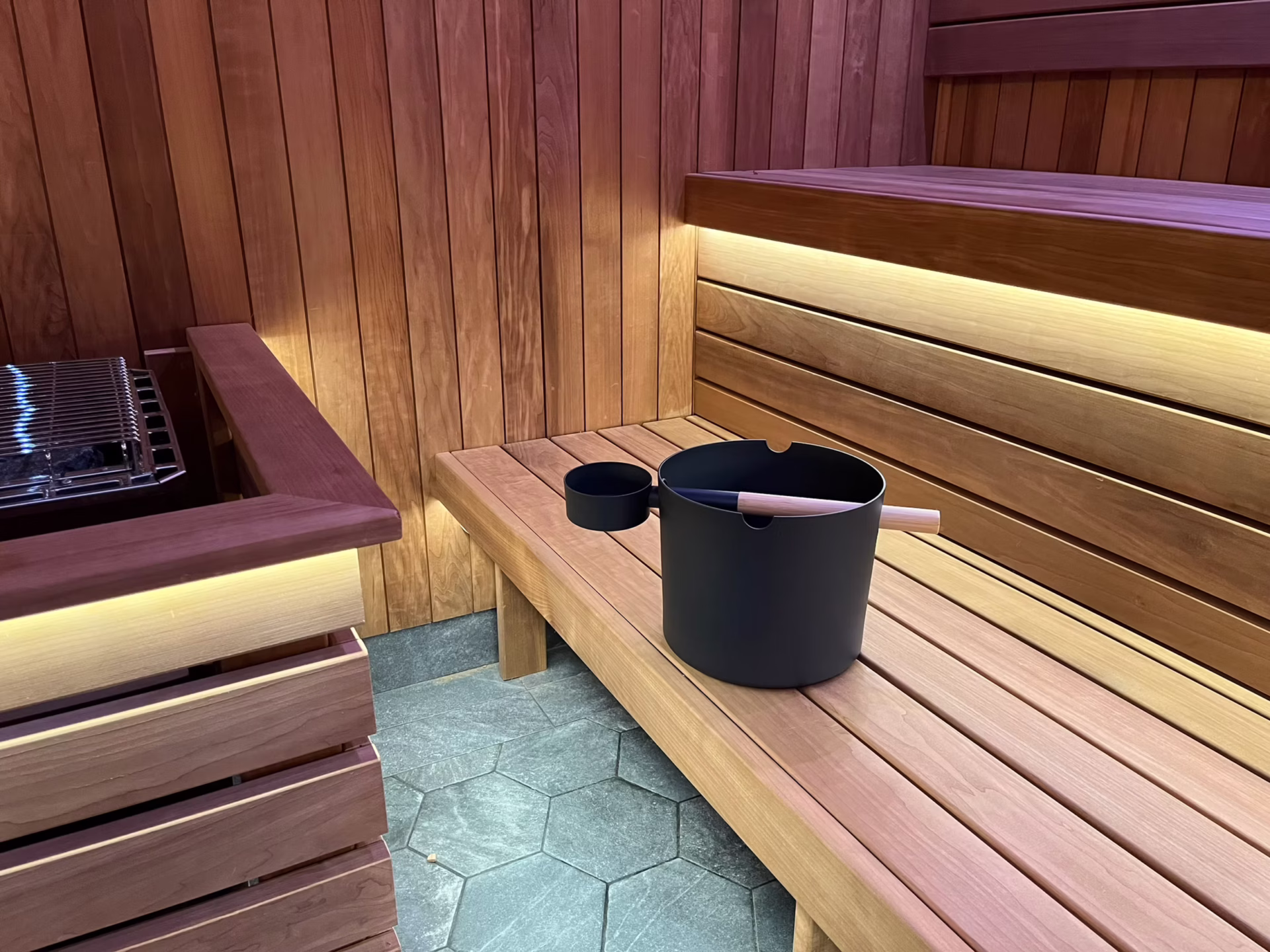 Interior of a wooden sauna with a bucket and ladle on the bench.