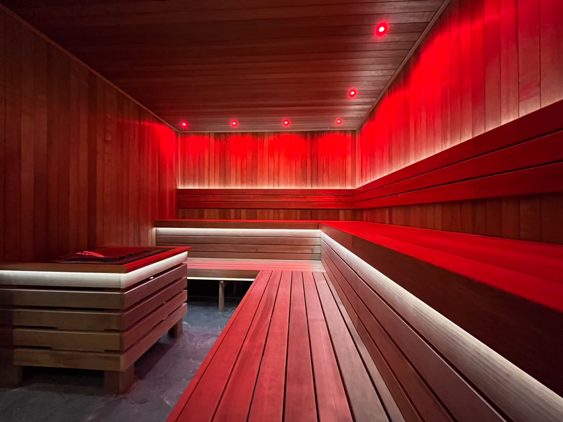 Modern sauna room with red ambient lighting and wooden benches.