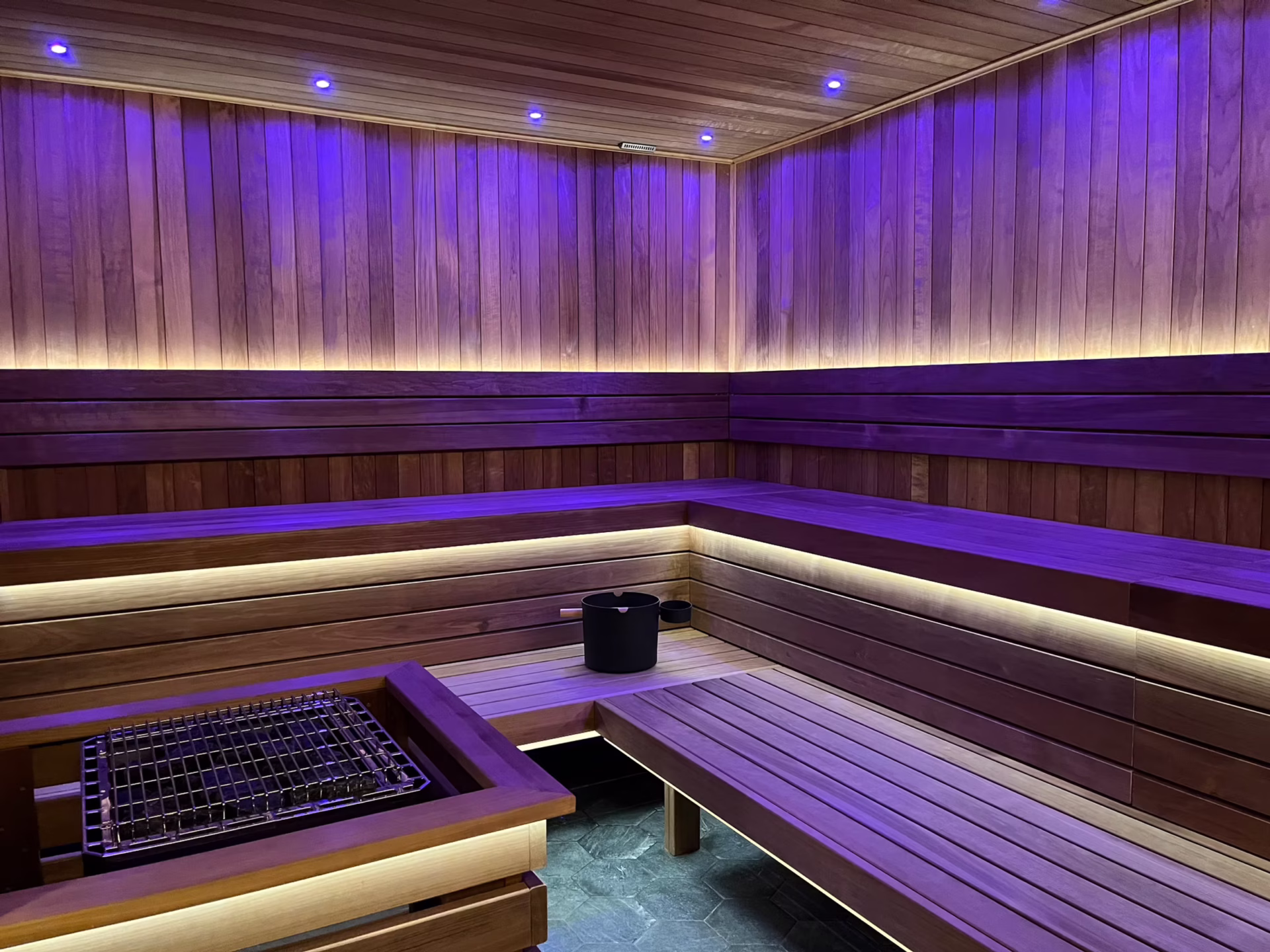 Modern sauna with wooden benches and ambient purple lighting.
