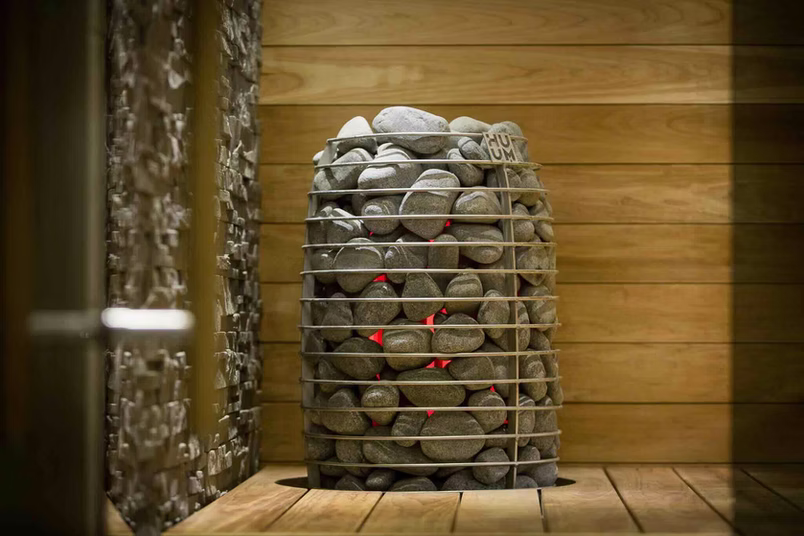 A cage filled with sauna stones inside a wooden sauna room.