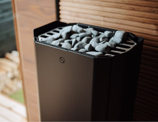 A modern sauna heater with stones on top inside a wooden sauna.