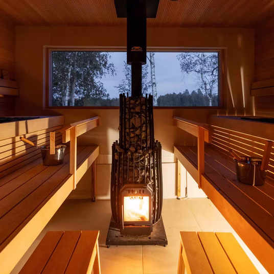 Cozy wooden sauna with a central stove and large windows.