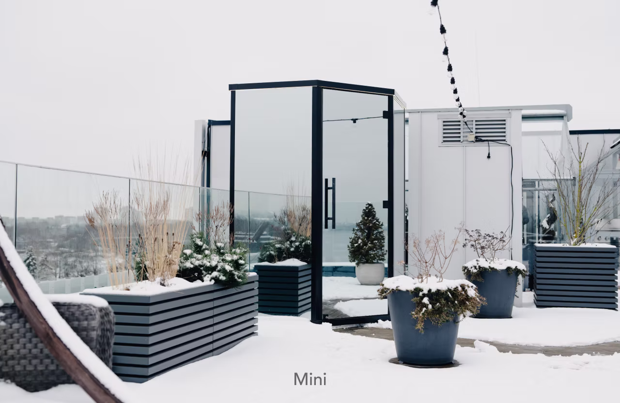 Modern glass door entrance with planters and string lights in a winter setting.