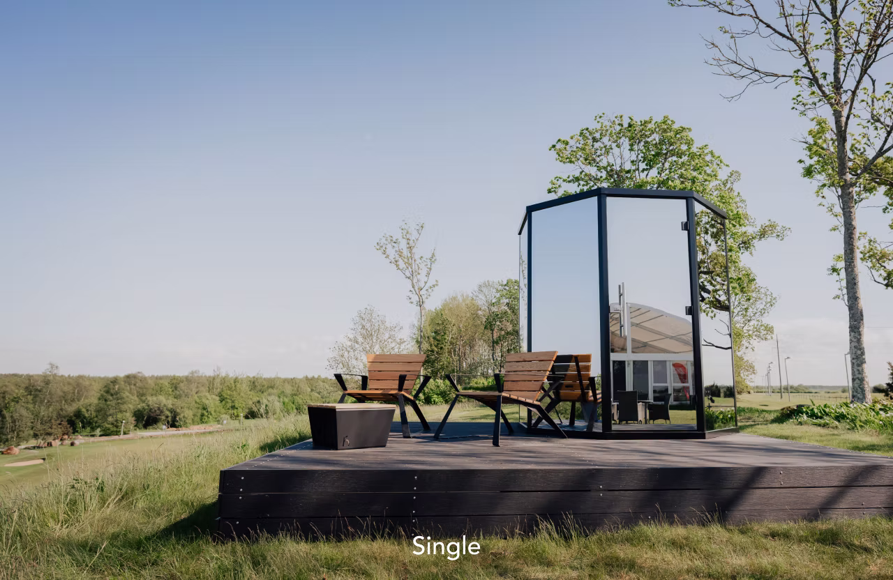 A modern glass bus stop with benches in a rural area under a clear sky.