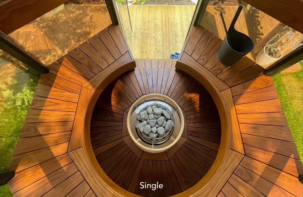 Top view of a circular wooden sauna stove filled with stones.