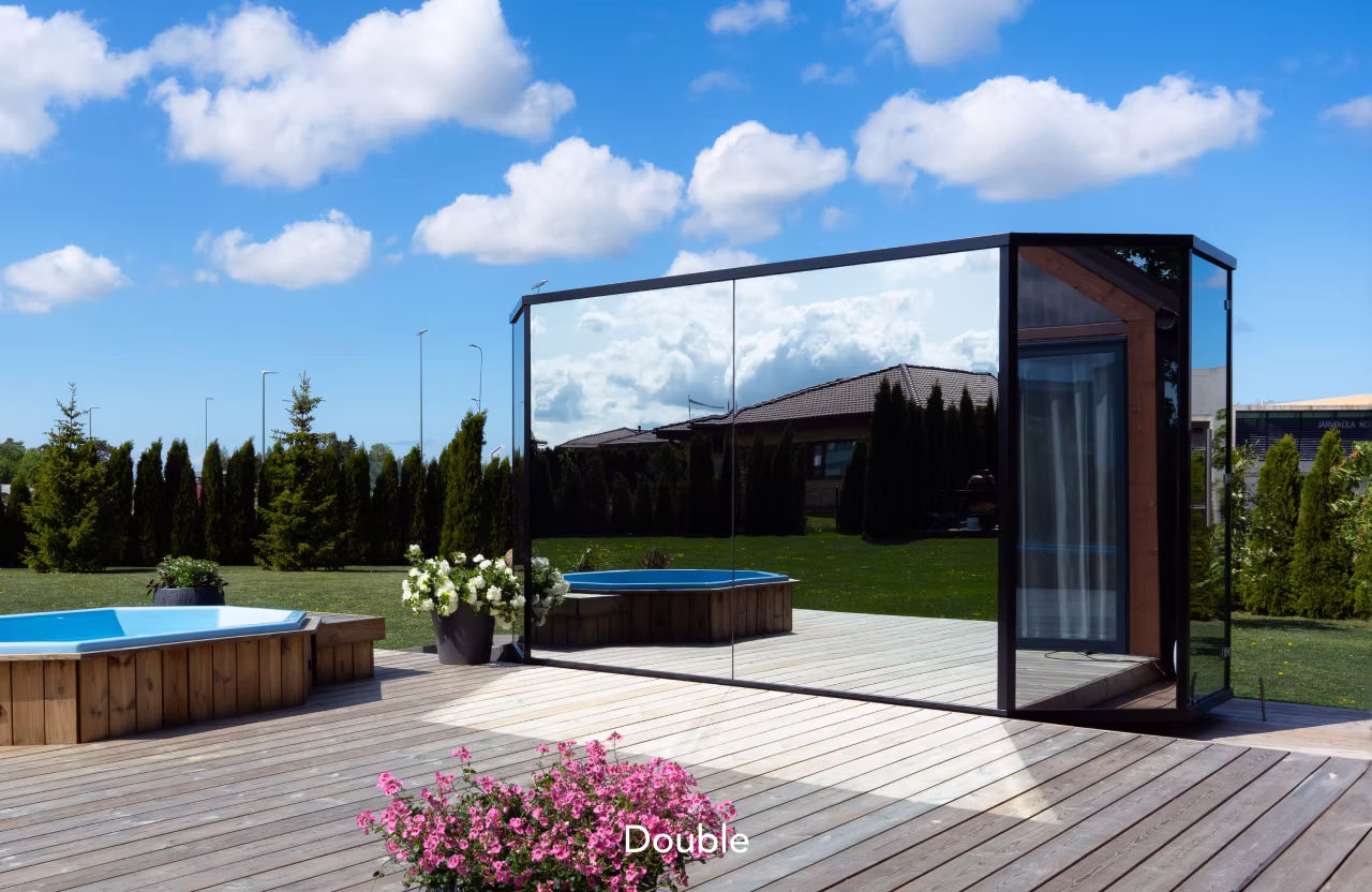 Modern patio with wooden deck, seating, and glass enclosure under a blue sky.