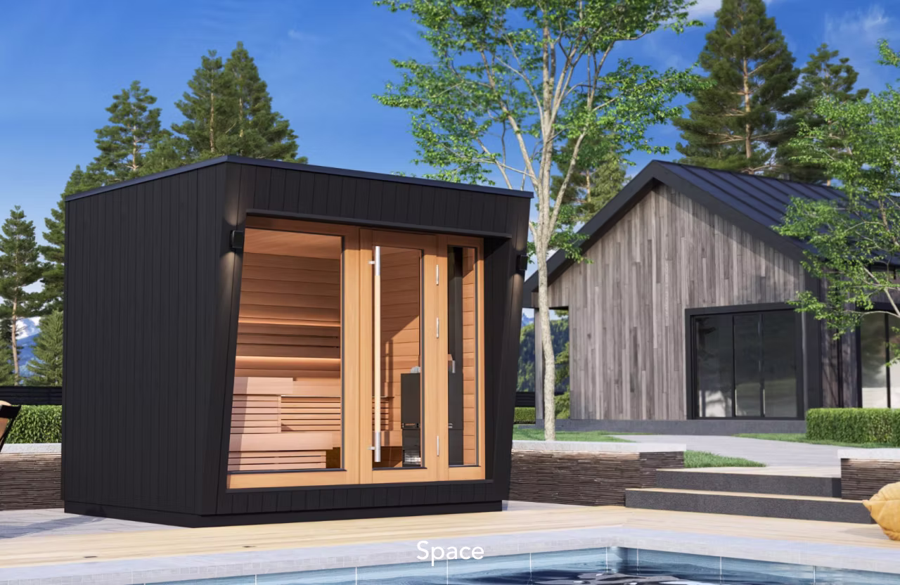 Modern sauna cabin beside a pool with a wooden house in the background.