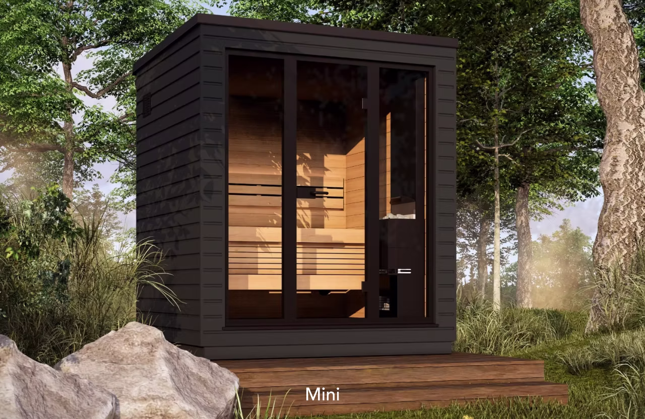 A small, modern wooden cabin in a forest setting.