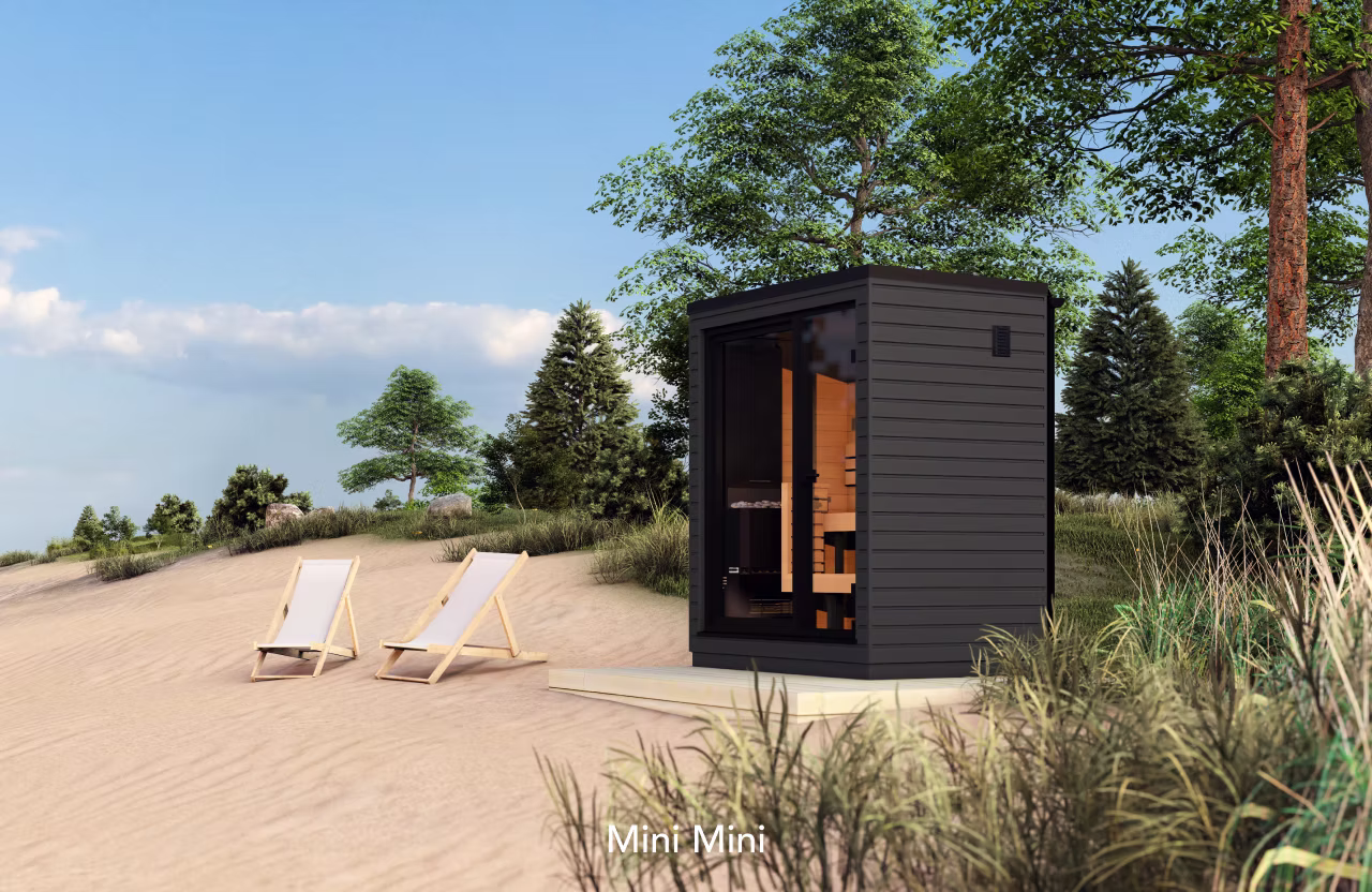 A modern black sauna cabin on a sandy beach with lounge chairs nearby.